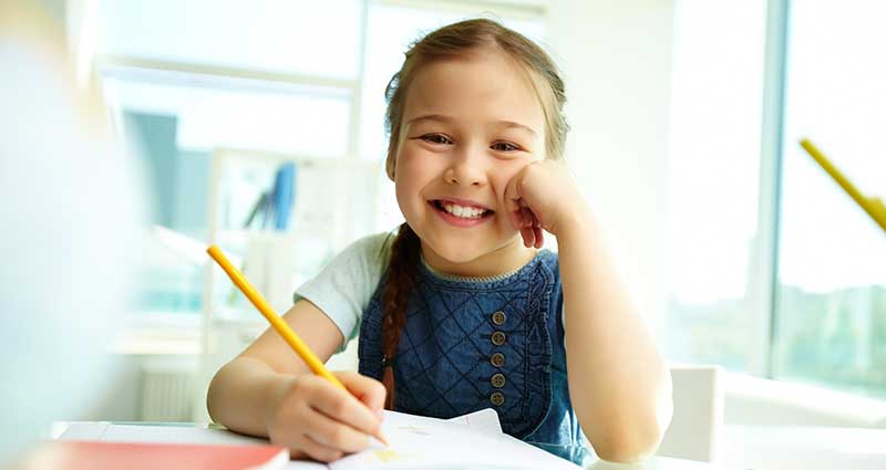 Child smiling while holding pencil at school desk
