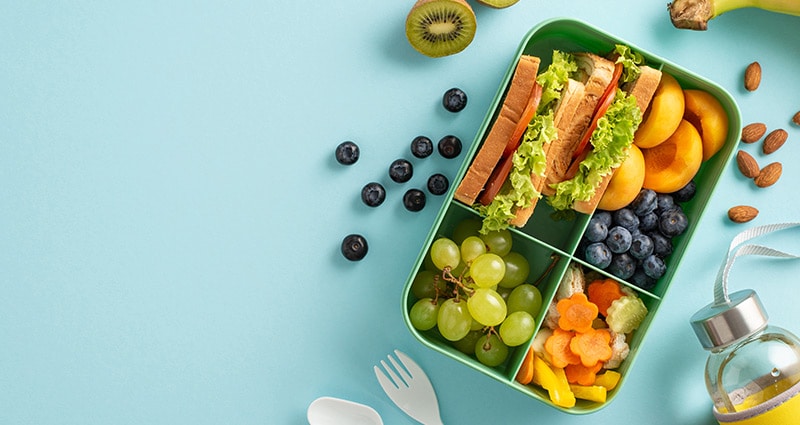 lunchbox with fruit and sandwich on a light blue background