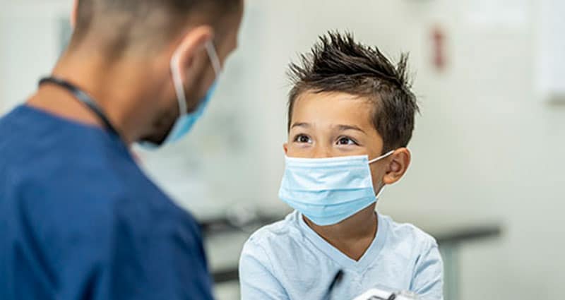 child in face mask speaking with medical professional