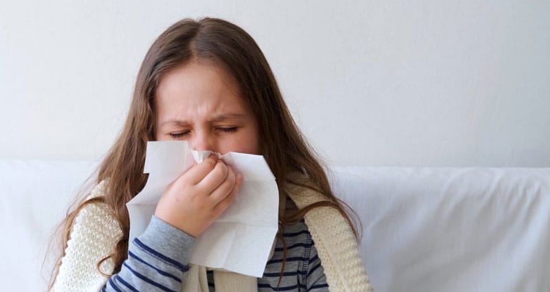 girl sneezing into tissue