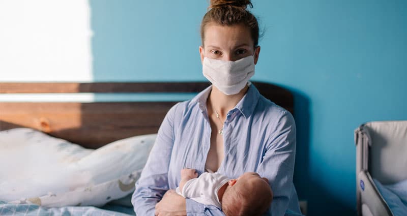 woman holding a baby and wearing a face mask
