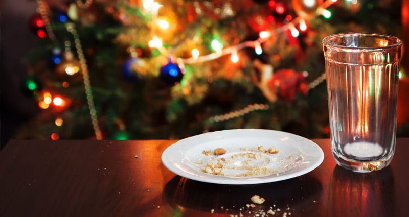 Holiday scene of leftover cookie crumbs on a platter next to nearly empty glass of milk
