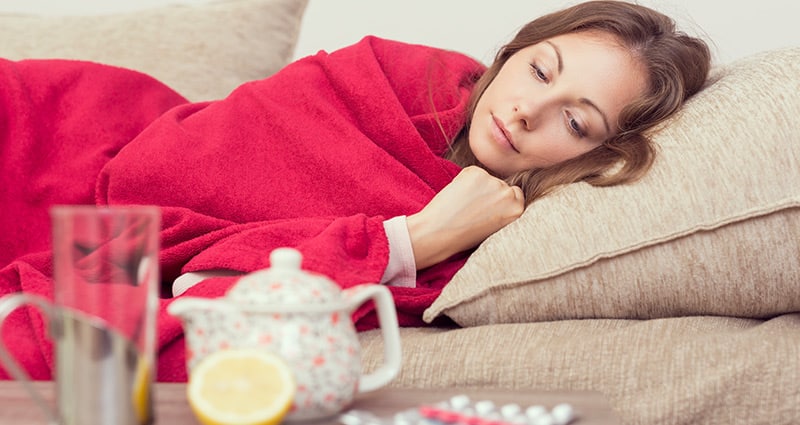 woman resting on a couch wrapped in red blanket