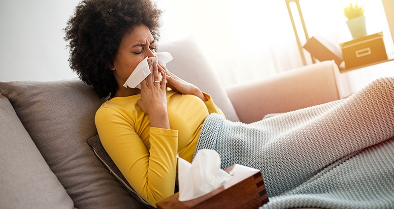 woman blowing her nose while laying on a couch