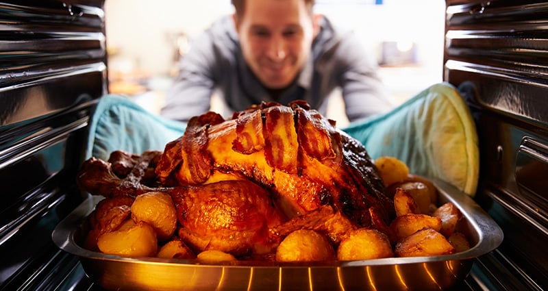 man taking roast turkey out of the oven