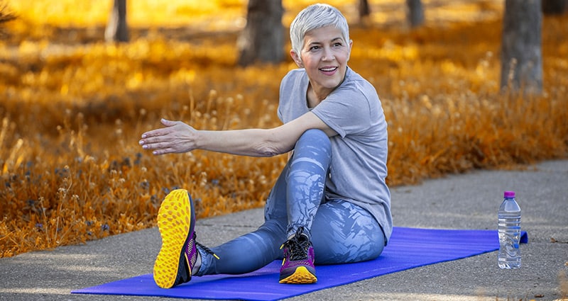 older woman stretching on yoga mat outside