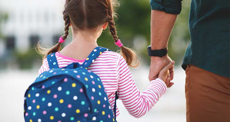 adult holding hands with a child carrying a backpack