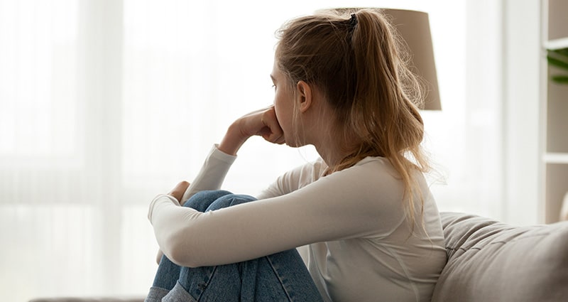 teen girl sitting on a couch looking out a window