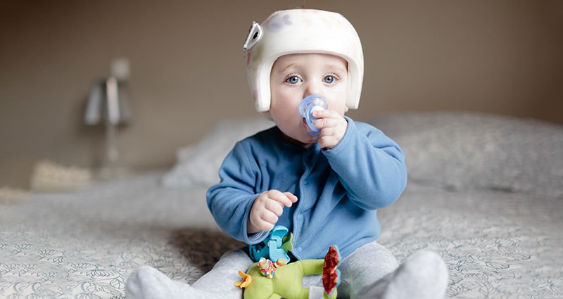 baby wearing helmet playing with toys and pacifier