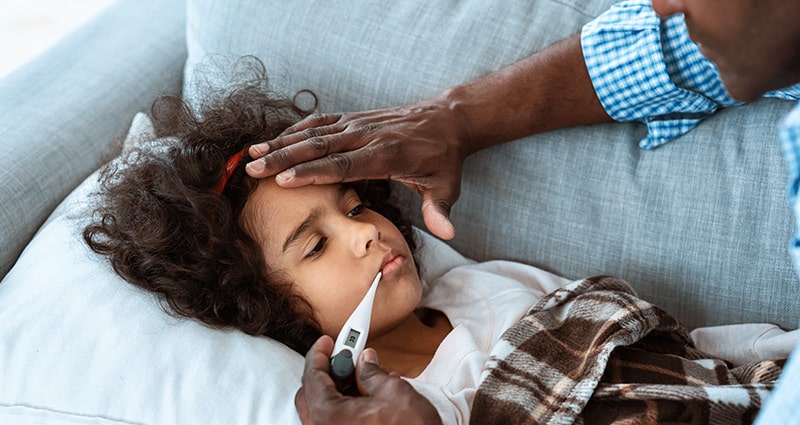 child on couch having temperature checked