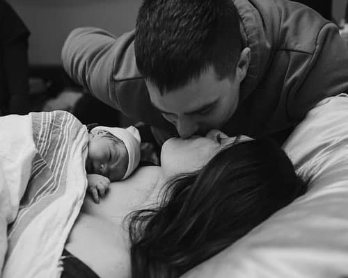mother and father kissing above newborn shortly after delivery
