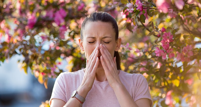 sneezing woman in front of flowering tree