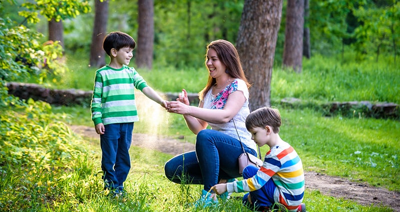 woman putting bug spray on two kids