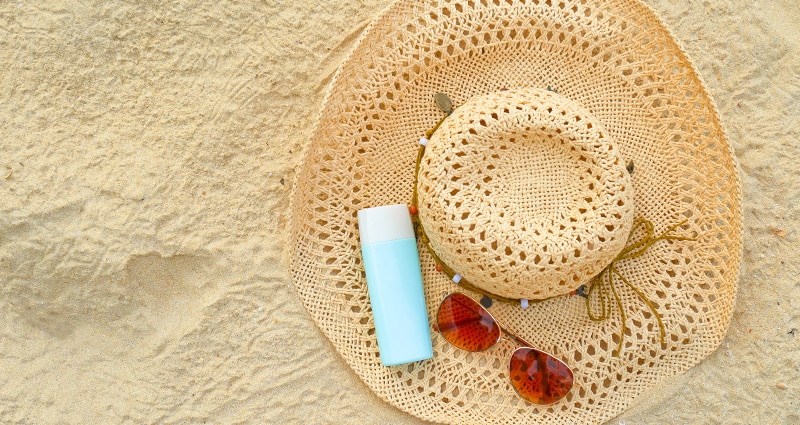 sun hat, sunscreen and sunglasses on sand