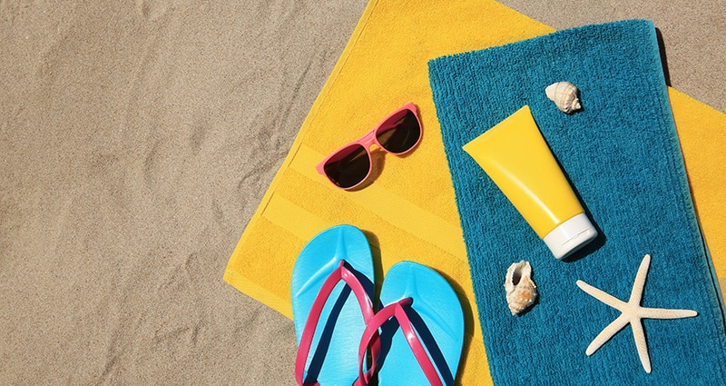 sunscreen, flipflops, sunglasses and towels on sand