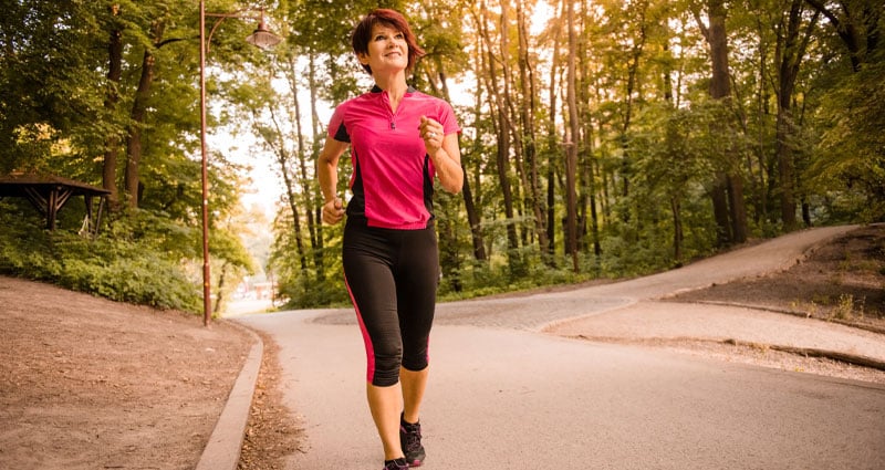 woman in exercise clothes running down a forest road