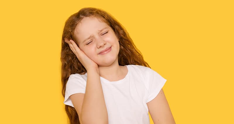 young girl holding her ear and wincing in pain