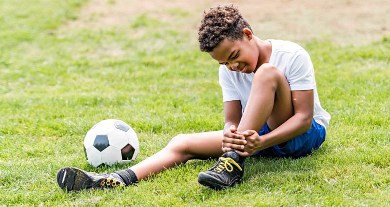 young soccer player grabbing injured leg