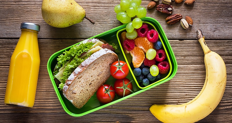 lunch box with sandwich and fruit, bottle of juice on wood background