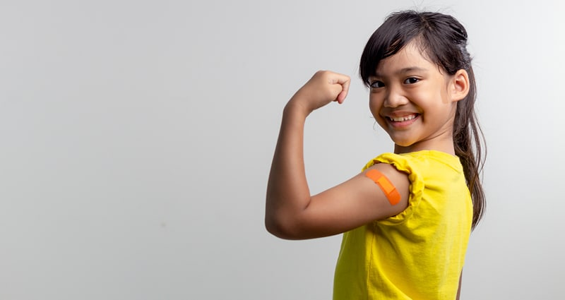 girl in yellow shirt showing off her bandaid after vaccination