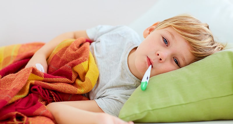 child on green pillow with thermometer in mouth