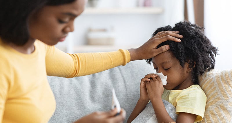 mom looking at thermometer with her hand on daughter's head