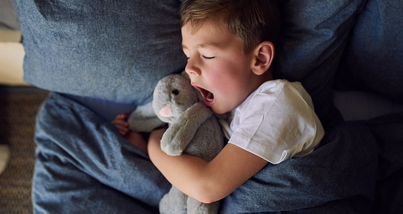 child in bed holding stuffed animal