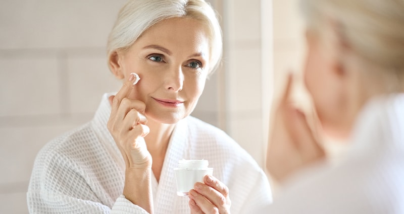 woman putting skincare on while looking in mirror