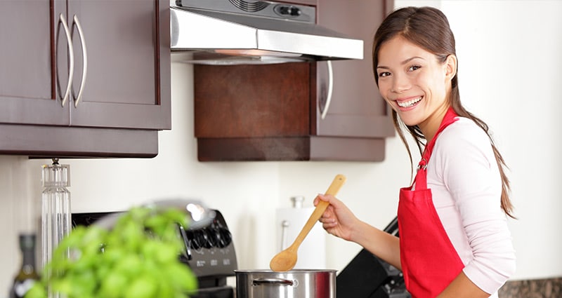 smiling woman in red apron stirring pot at stove