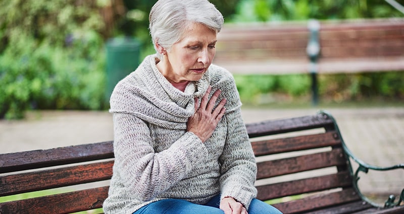 woman clutching chest sitting on park bench