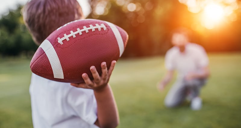 boy throwing football to kneeling dad in background