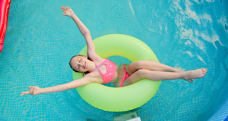 girl floating in pool in bright pink bathing suit