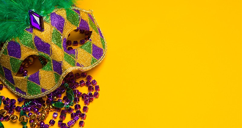 mardi gras mask and beads on yellow background