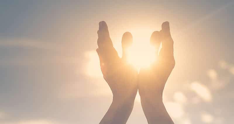 hands lifted in praise while sunlight streams through