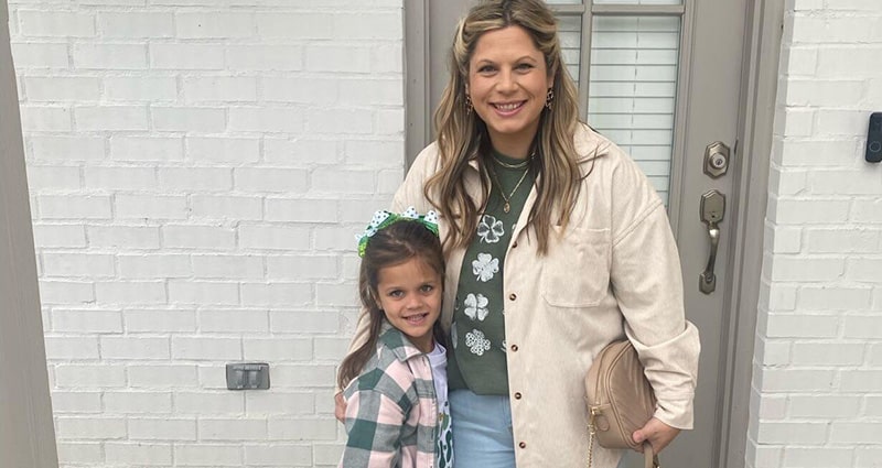 A woman and a little girl stand in front of a doorway. They are smiling.