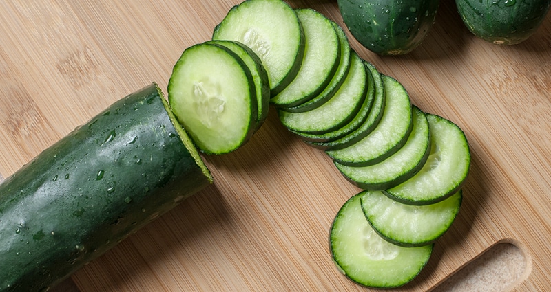 A green cucumber, partially sliced, lies on a cutting board.