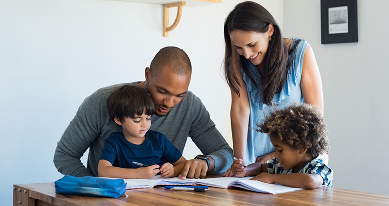 A man and a woman help two boys with their homework.